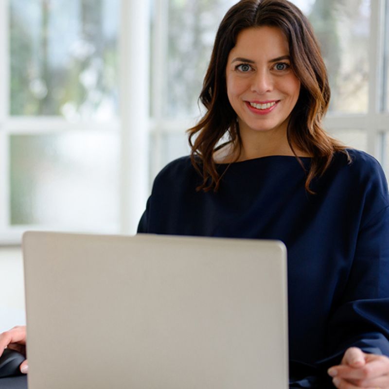 Melanie Schwarz - Coach für berufliche Neuorientierung - sitzt an ihrem Laptop und schaut in die Kamera.